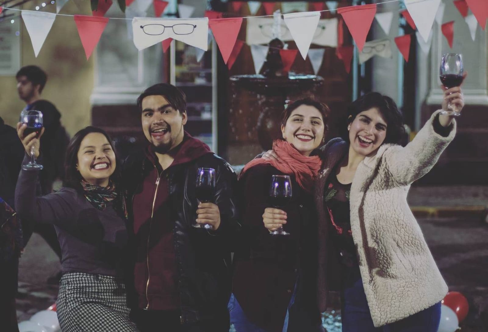 Four members of the third-edition team toast with red wine under red and white bunting.
