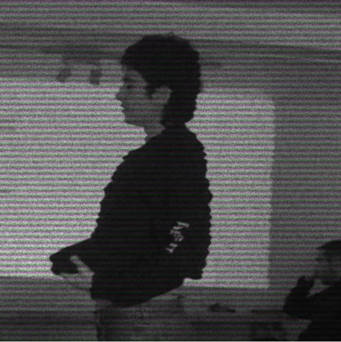 Gabriel in profile, in a dark sweater, behind a texture of gray and violet scan lines.