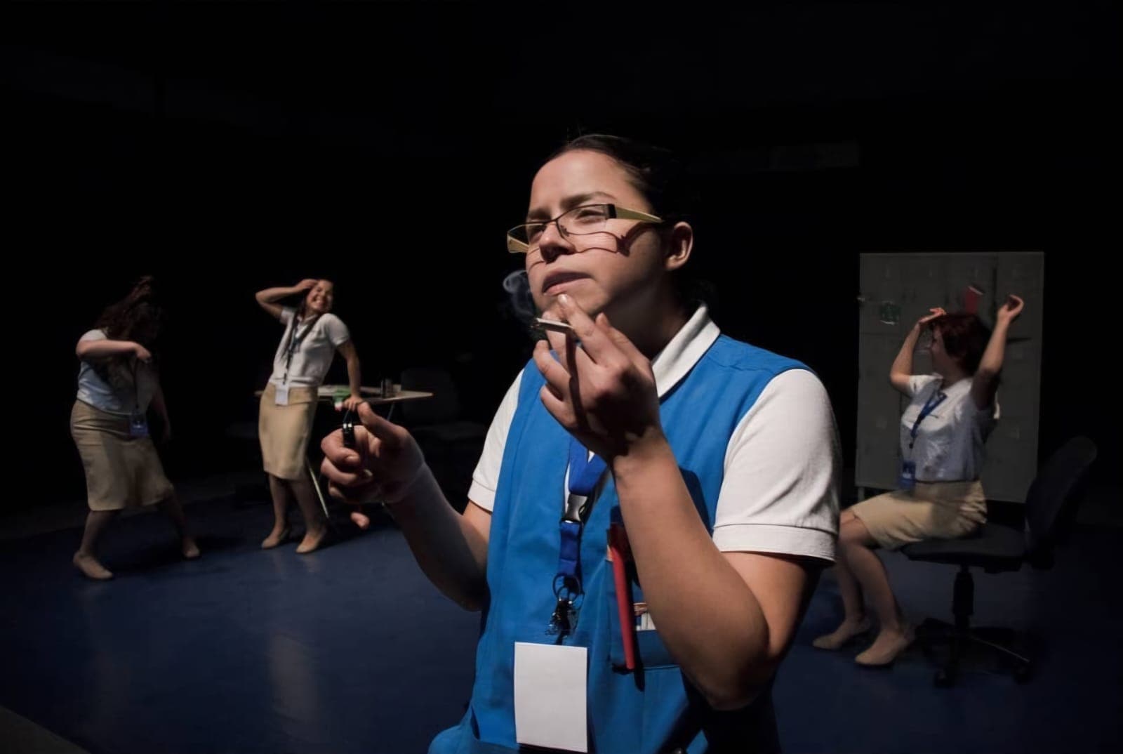 A cashier in a blue apron smokes in the foreground while three colleagues dance behind.