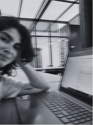 Black-and-white photo of Gabriel smiling, head resting on one hand, next to a laptop.